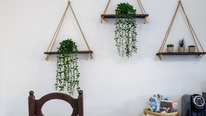 A wooden chair with a woven seat, a wooden desk, and three hanging plant shelves against a white wall. - Casa Isleña Inn (Rincon)