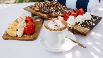 En frukostuppläggning med en kopp kaffe, en tallrik med frukt och ett bakverk på en träbricka.