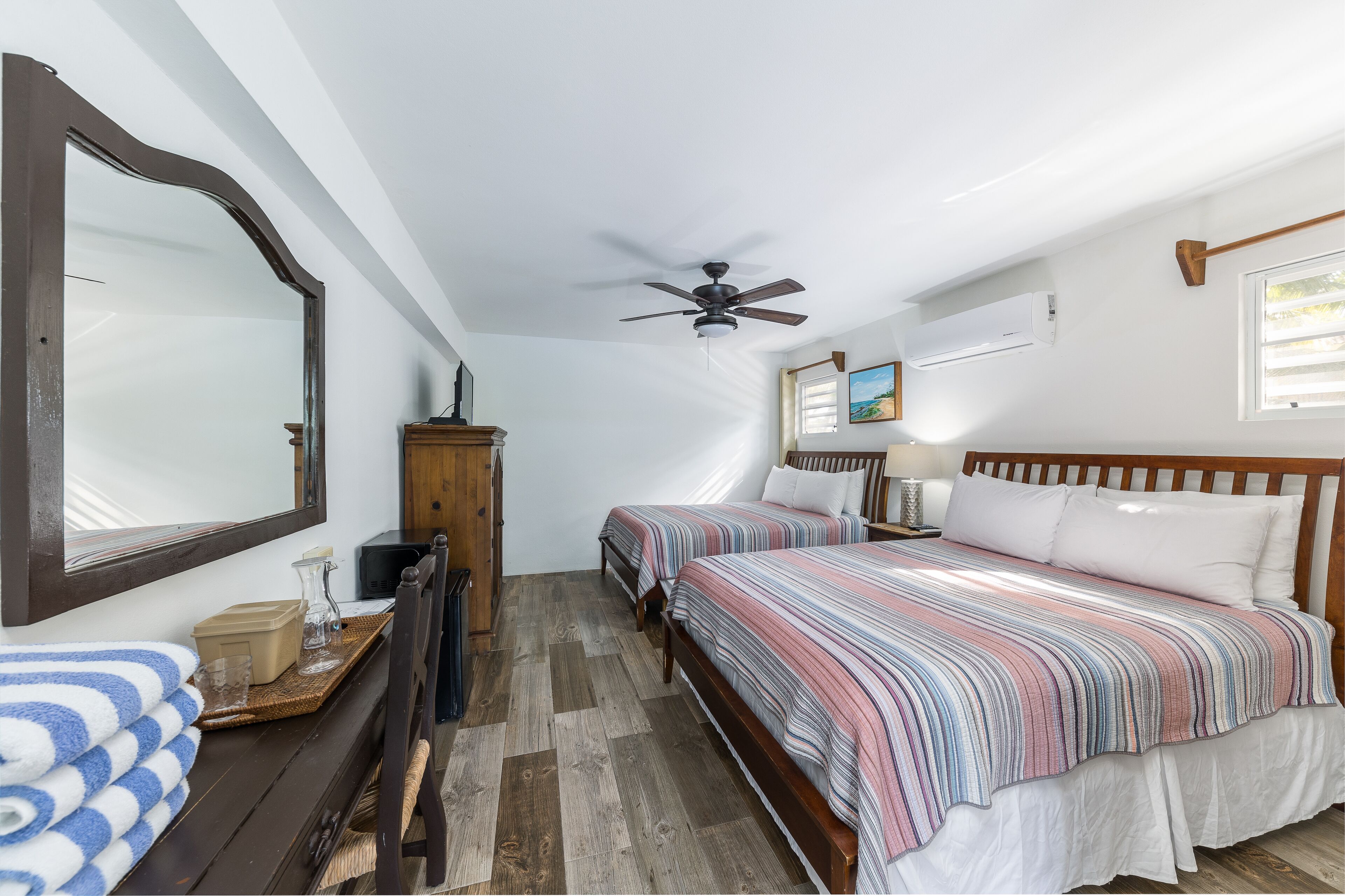 A bedroom with two beds, a ceiling fan, a large mirror, and a wooden dresser.