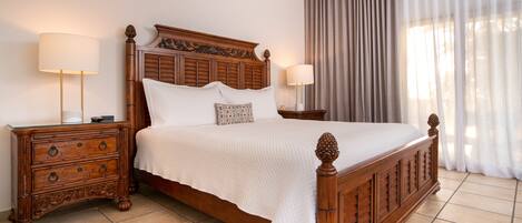 A wooden four-poster bed with a quilted white bedspread, two nightstands with lamps, and a large window with sheer curtains.