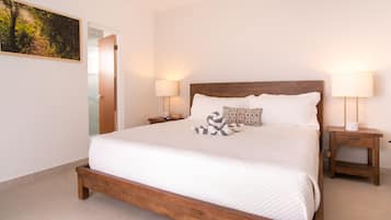 Une chambre à coucher avec un lit en bois, du linge de lit blanc, deux lampes de chevet, une table de chevet, un jouet en peluche et un tableau accroché au mur.