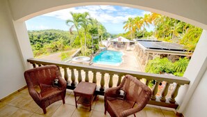 A balcony with wicker chairs and a view of a pool and tropical landscape. - Lazy Parrot Inn (Rincon)