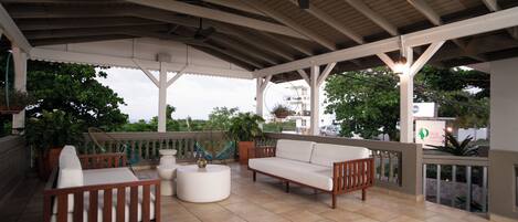 A covered outdoor seating area with a ceiling fan, a white sofa, and a wooden bench.