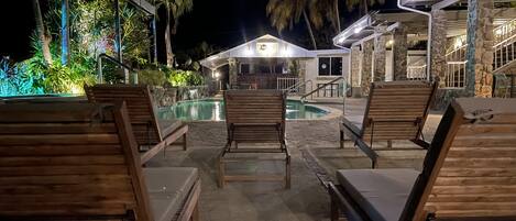 Zona de piscina con sillones de madera y un edificio de piedra al fondo.