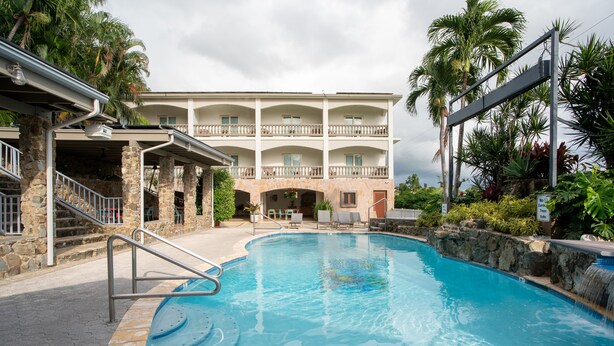 A swimming pool with a stone border, a multi-story building with balconies, and a staircase leading to the building.