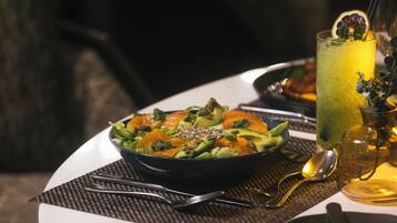 A dining table with a bowl of salad, a glass of drink, and cutlery.