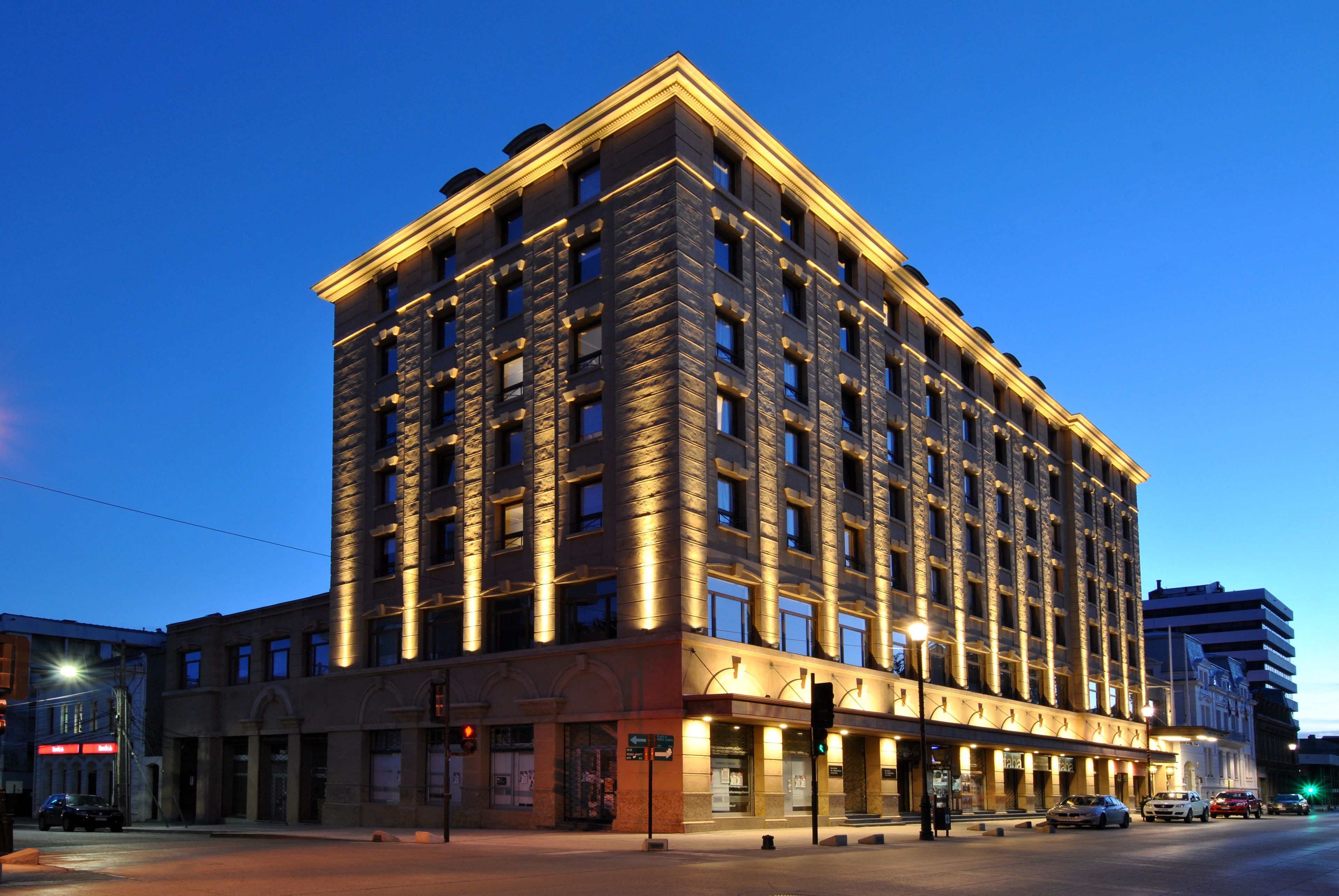 A multi-story hotel with a classic architectural design, featuring a prominent corner location, large windows, and a well-lit facade.