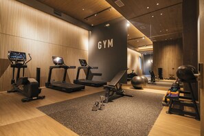 A modern gym with treadmills, elliptical machines, a bench, and various weights.