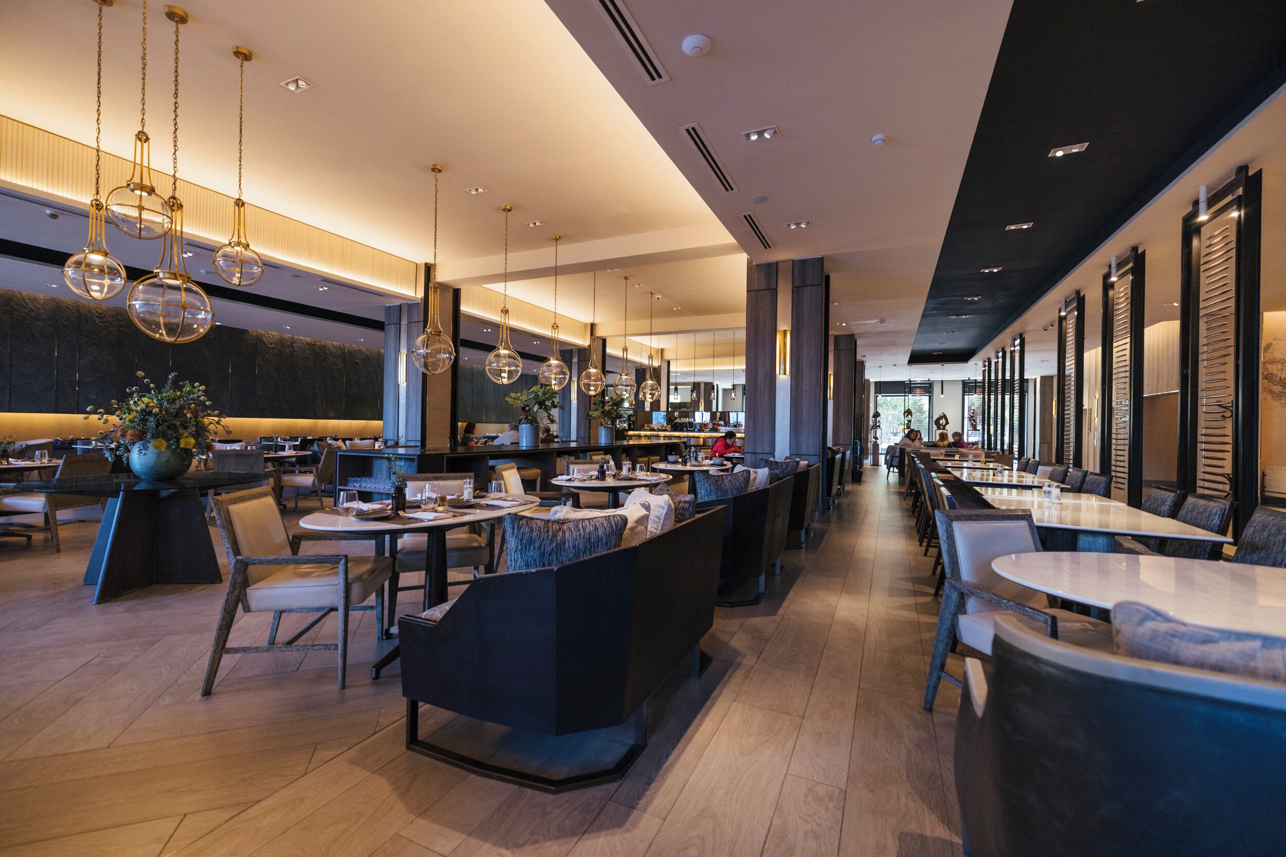 Un restaurante moderno con techos altos, iluminación colgante y una combinación de asientos tipo cabina y mesas.