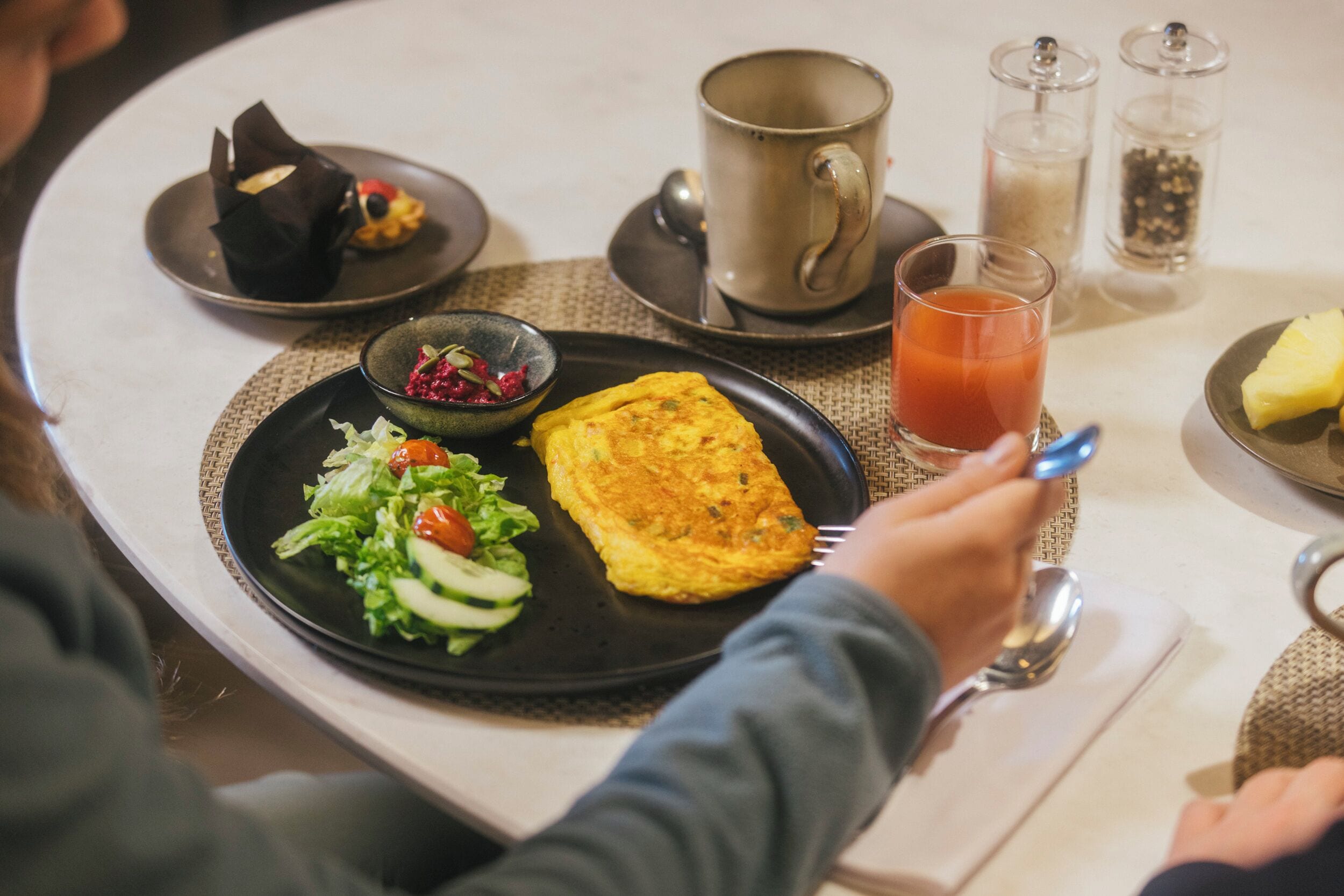 Una mesa de comedor con un plato de comida, una taza y condimentos.