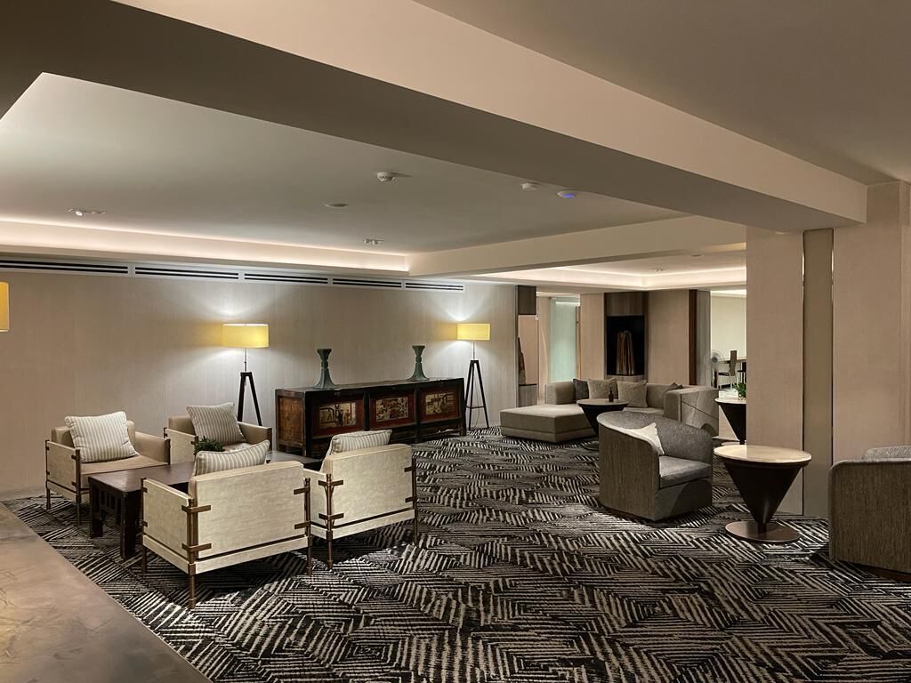 Un moderno vestíbulo de hotel con alfombra de diseño geométrico, varias zonas de estar e iluminación ambiental.
