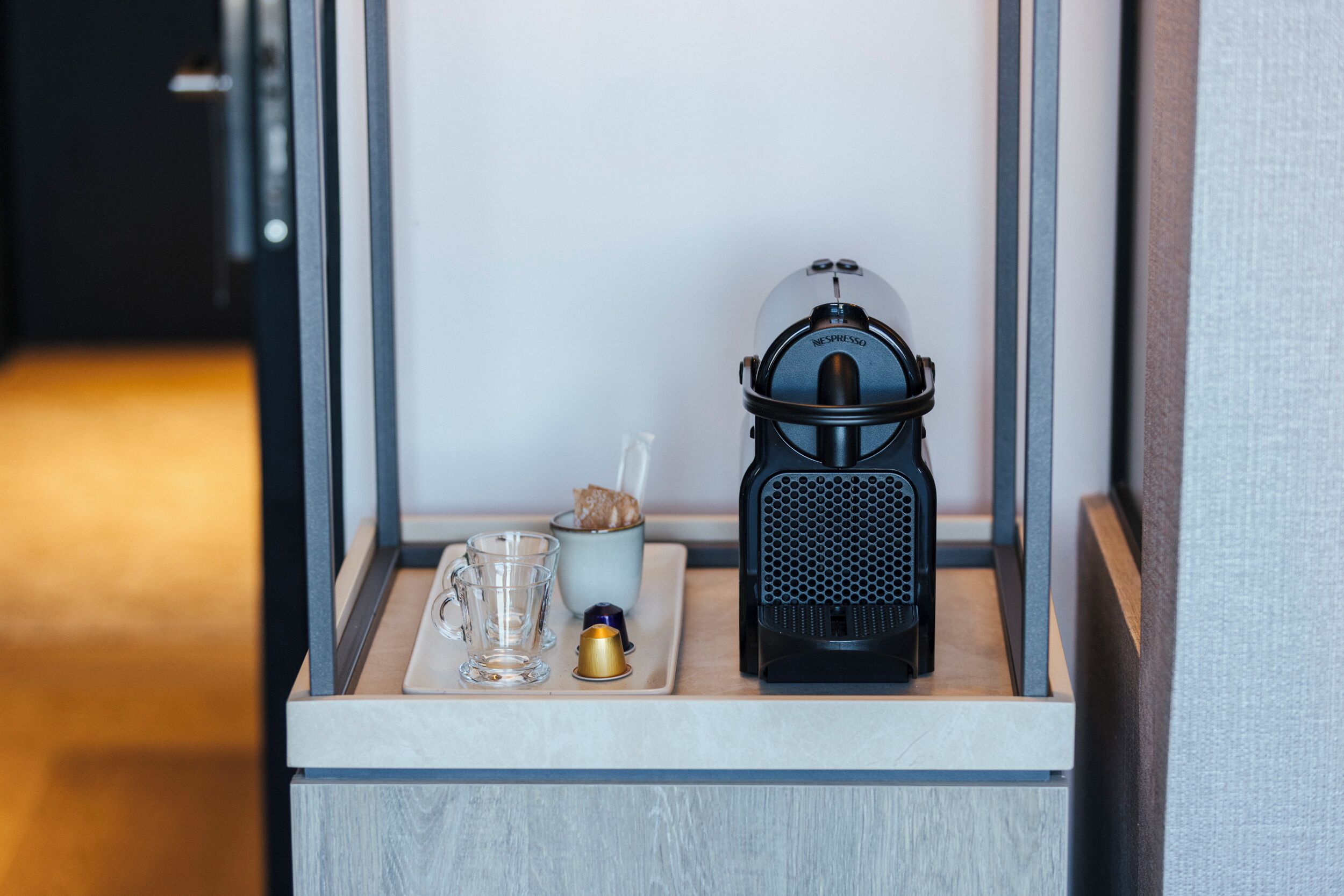 A coffee maker, a glass, and a cup on a tray in a hotel room.