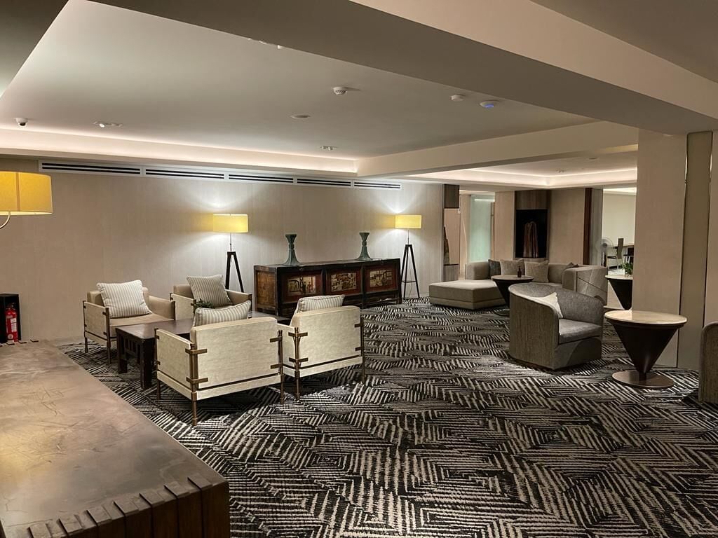 A modern hotel lobby with a patterned carpet, sofas, a coffee table, and a side table.