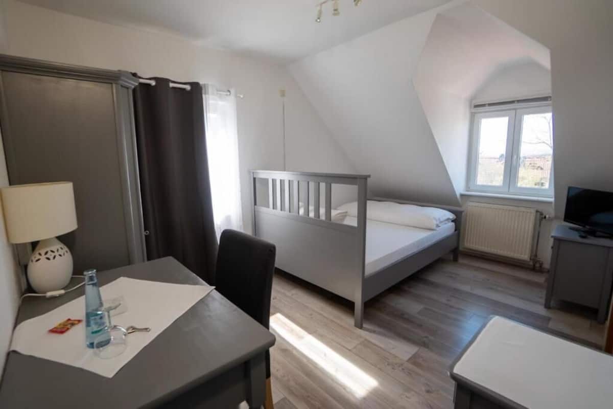 A room with a bed, a desk, a chair, a lamp, a window, and a radiator.