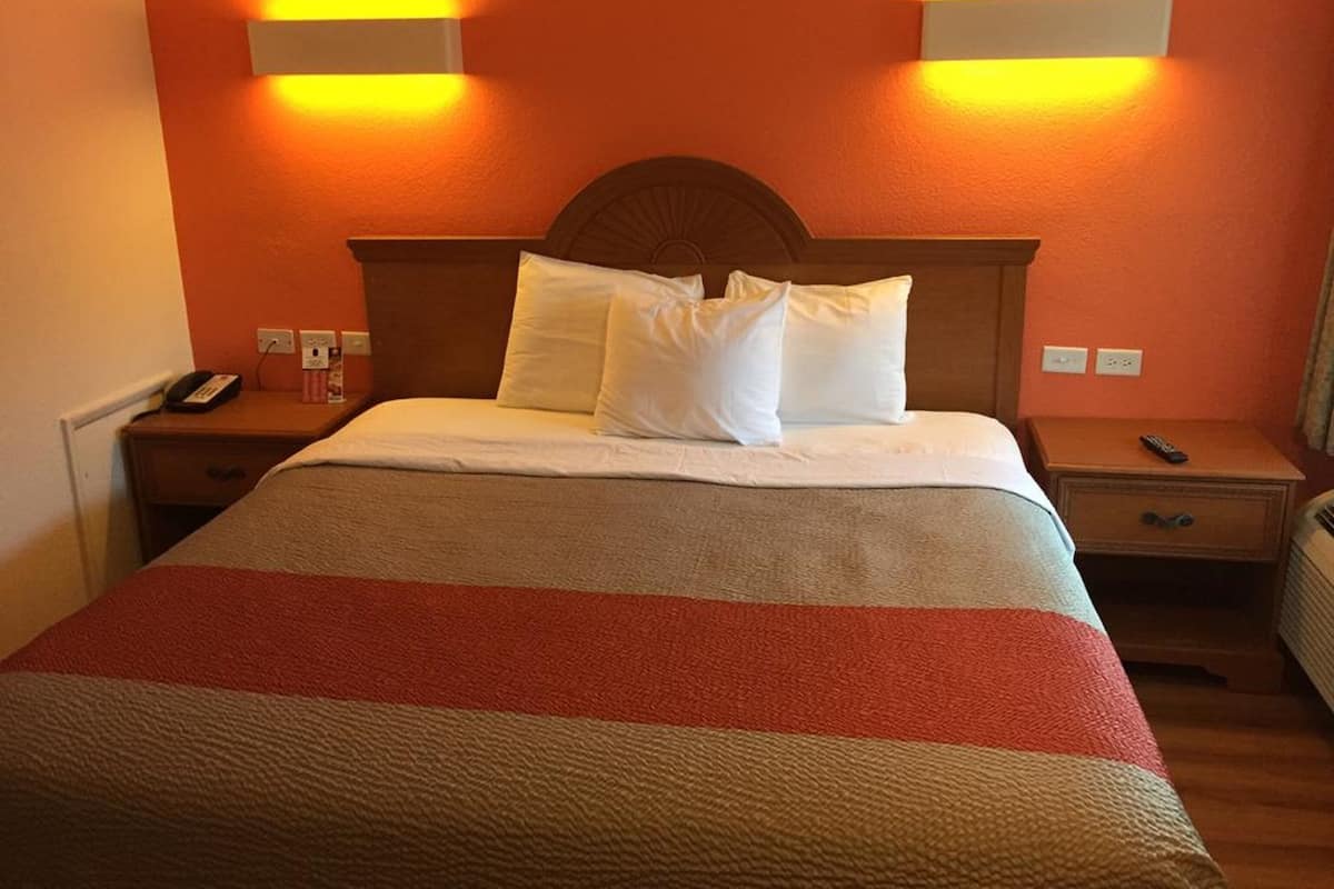 A hotel room with a bed, two bedside tables, a nightstand, and two wall-mounted lights.