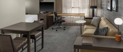 A hotel room with a dining table, a sofa, a TV, a desk, and a lamp.