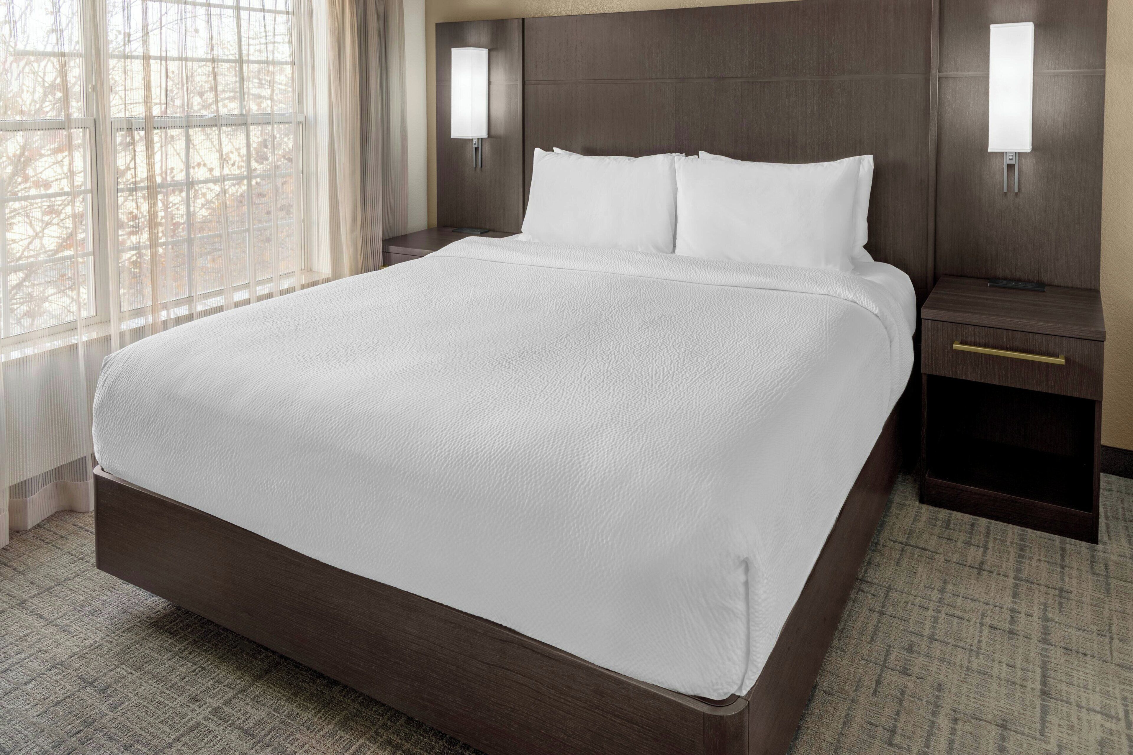A hotel room with a large bed, two bedside tables, and a window with curtains.