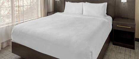 A hotel room with a large bed, two bedside tables, and a window with curtains.