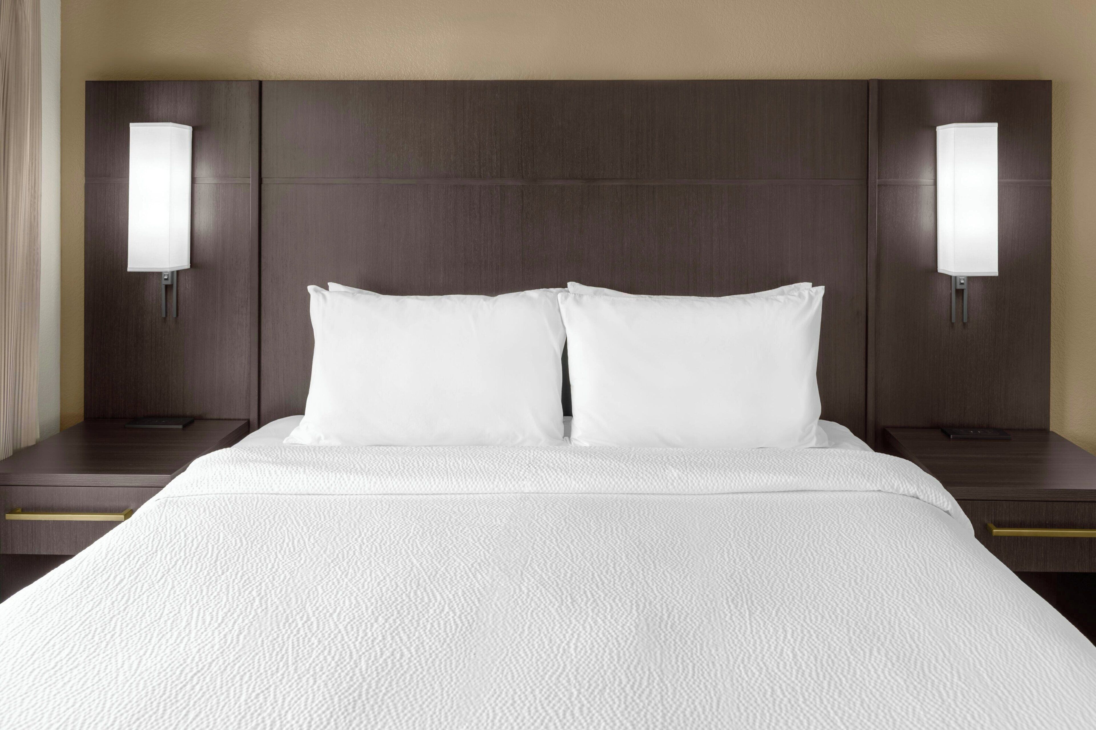 A hotel room with a large bed, two bedside tables, and wall-mounted lamps.