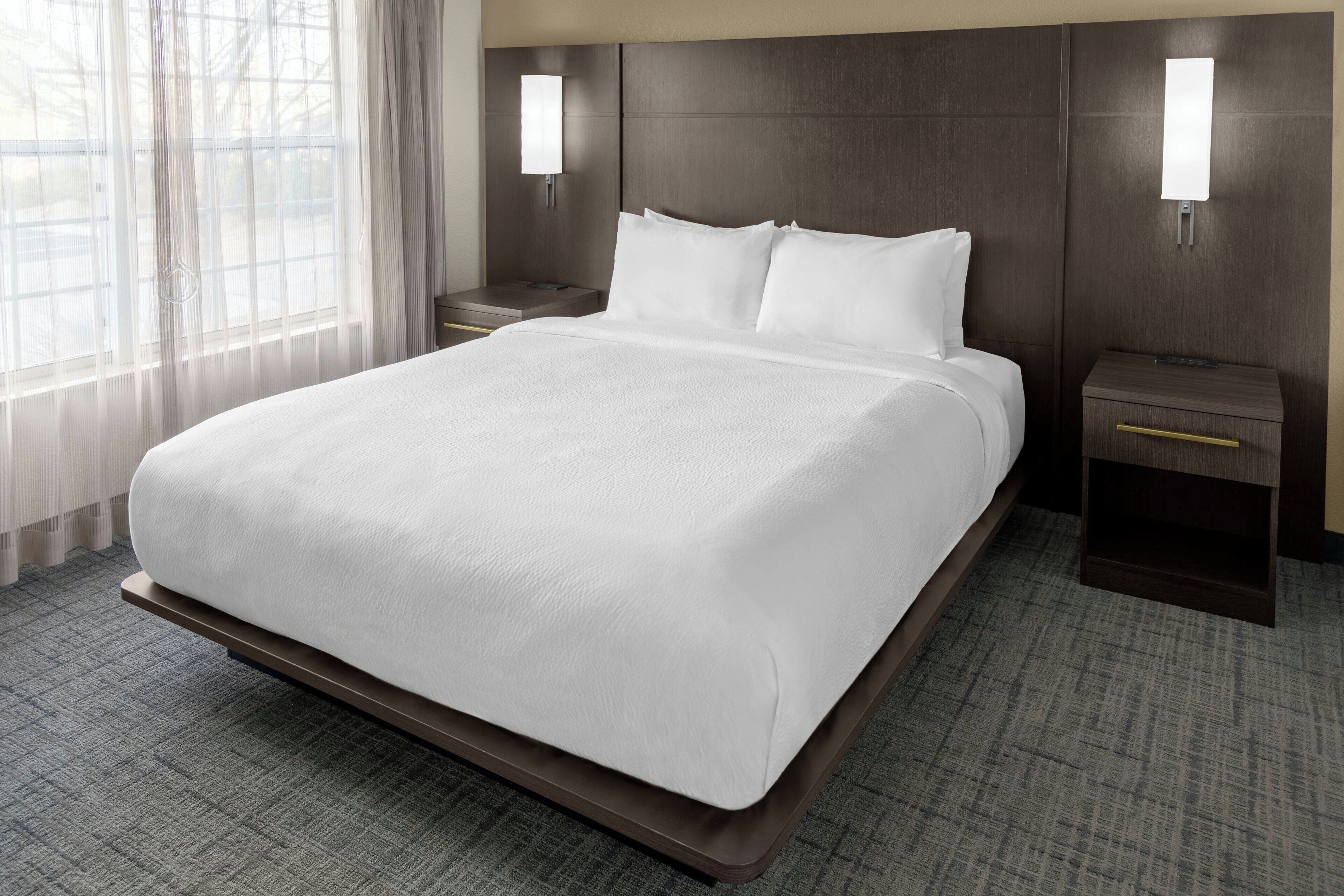 A hotel room with a large bed, a nightstand, a bedside table, and a wall-mounted light fixture.