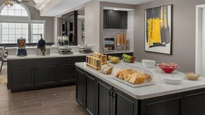 Une cuisine moderne dotée d’un grand îlot central, de meubles de rangement aux couleurs sombres et de divers produits alimentaires exposés sur le plan de travail.