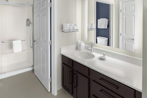 A modern bathroom with a white sink, dark cabinets, a glass shower enclosure, and a mirror reflecting the room. - Residence Inn by Marriott Albuquerque North (Albuquerque)
