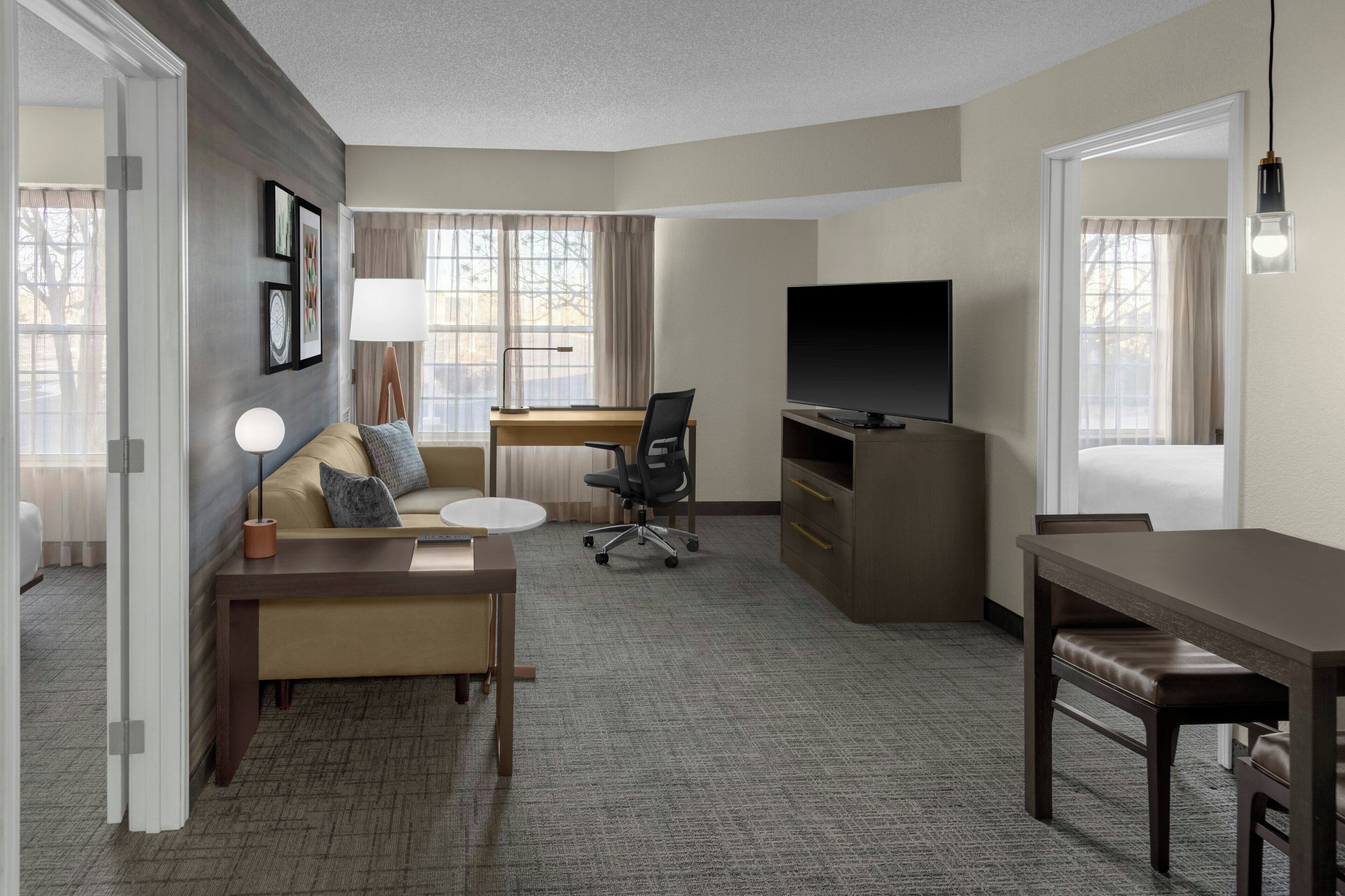 A hotel room with a sofa, a desk, a television, and a dining table.