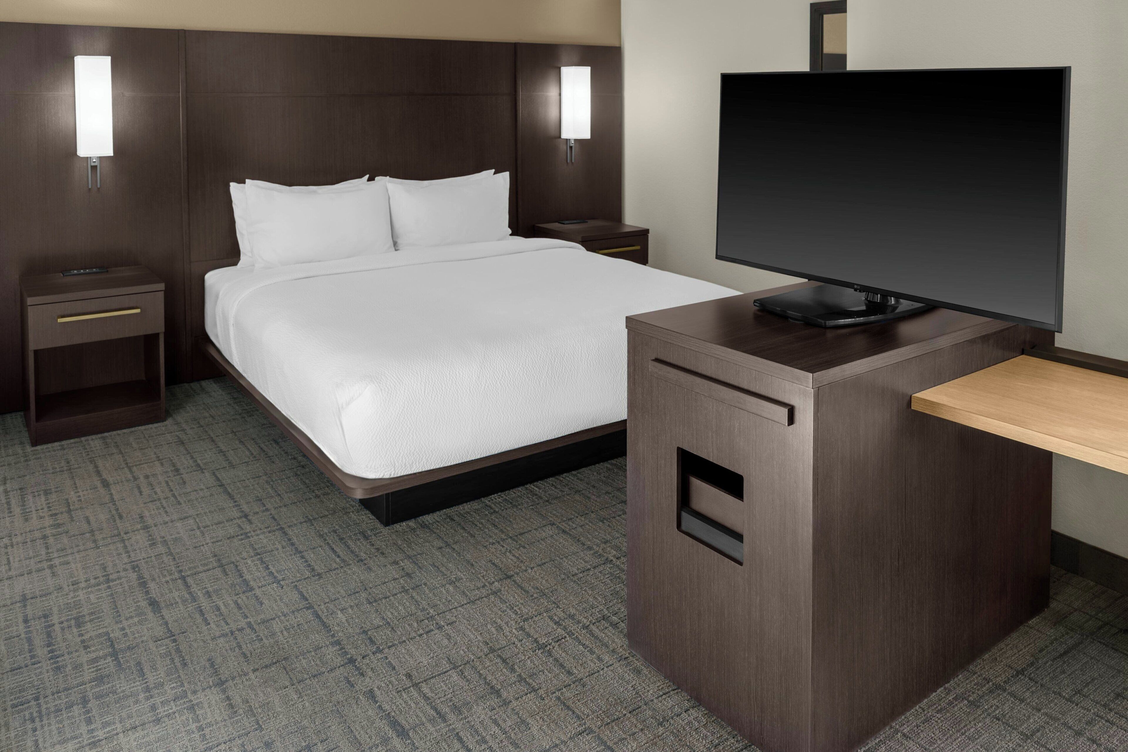 A hotel room with a large bed, bedside tables, a flat-screen TV, and a desk with a chair.