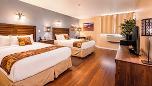 A hotel room with two beds, a desk, a television, a plant, and a painting on the wall.
