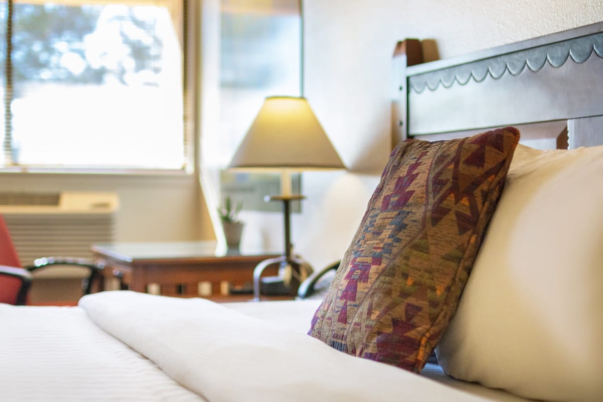 A hotel room with a bed, a chair, a lamp, and a window with blinds.