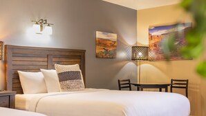 Une chambre d’hôtel avec une tête de lit en bois, un lit avec du linge de lit blanc, une table de chevet, une lampe et deux chaises.