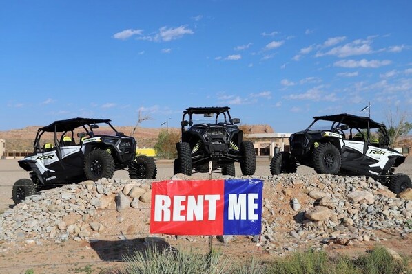 Three Polaris RZR off-road vehicles parked on a rocky terrain with a 'RENT ME' sign in the foreground.