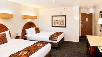 Habitación de hotel con dos camas, un escritorio, una silla, un cuadro en la pared y una puerta.