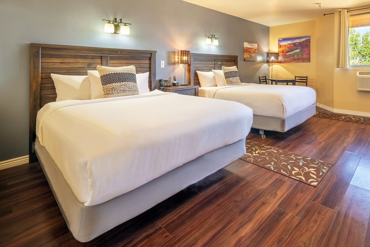 A hotel room with two beds, a desk, a chair, a lamp, and a painting on the wall.