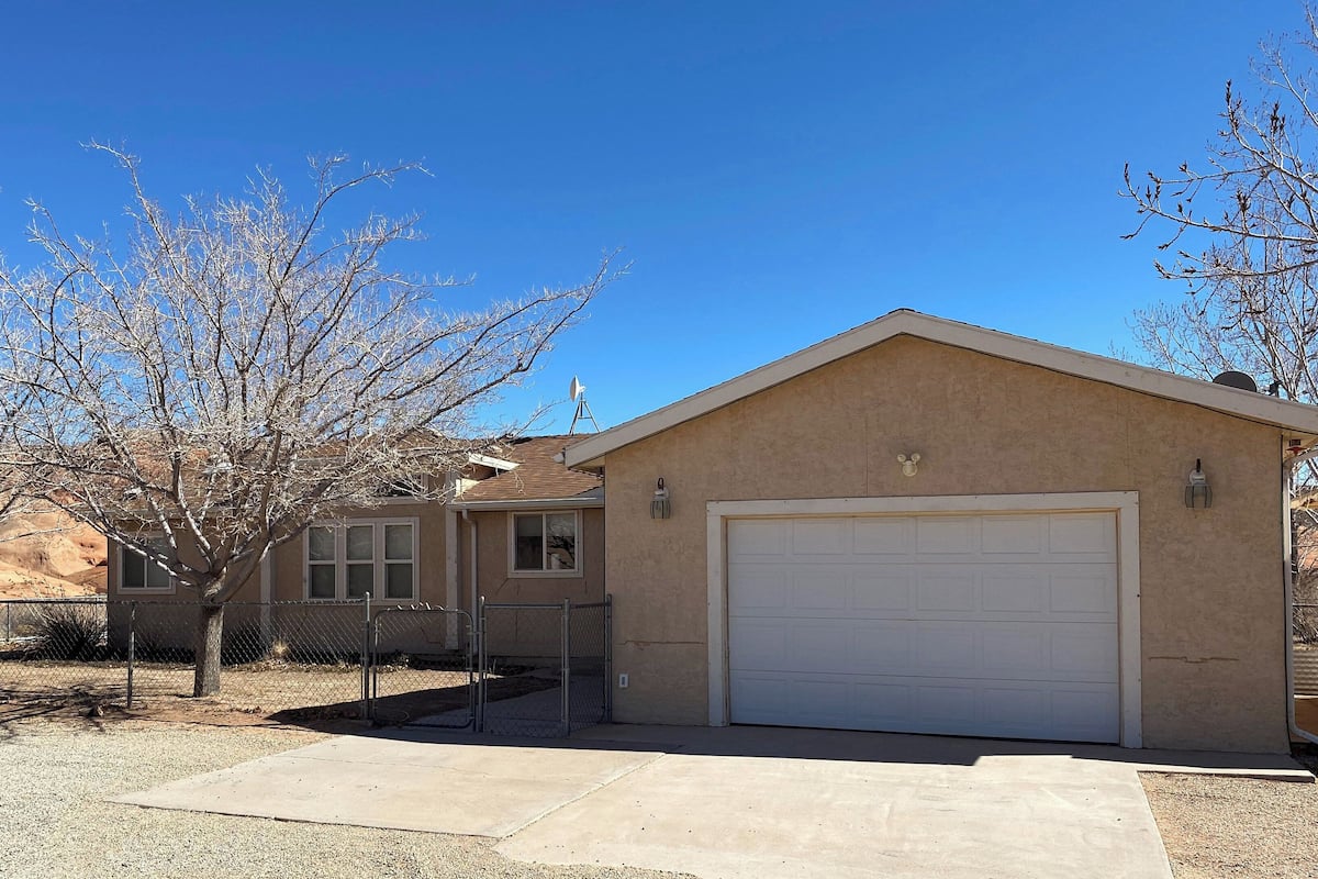 A single-story house with a garage, a fenced yard, and a tree with bare branches.