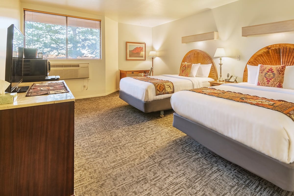 A hotel room with two beds, a desk, a television, and a window with blinds.