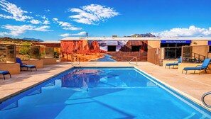 A swimming pool with lounge chairs, a restaurant named 'Mokis Restaurant,' and a mural of a desert landscape.