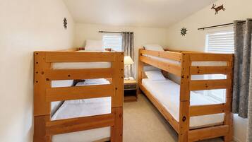 A room with two bunk beds, a nightstand with a lamp, and a window with curtains.