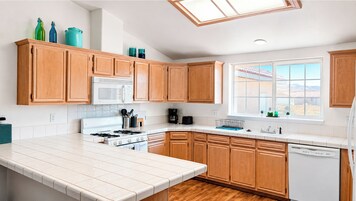 Una cocina moderna con armarios de madera, encimera blanca, estufa, microondas y ventana con vistas.