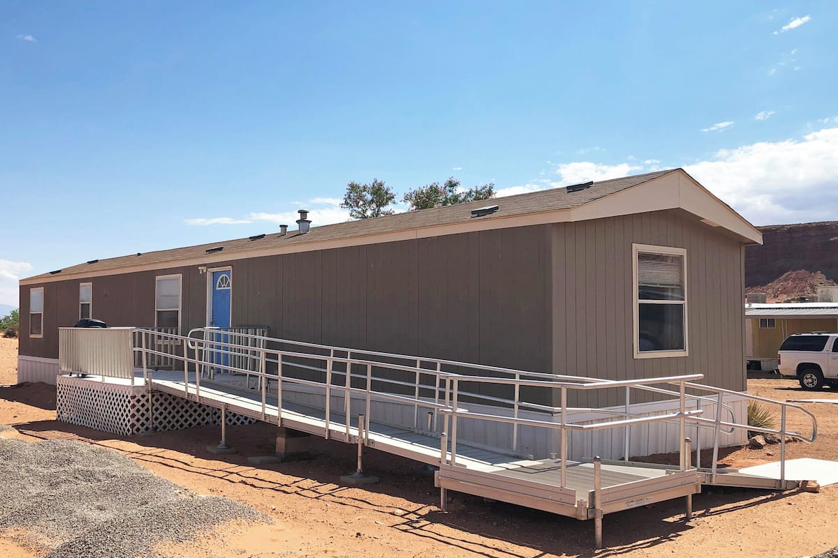 A small, single-story building with a blue door and a ramp leading to a covered outdoor area.