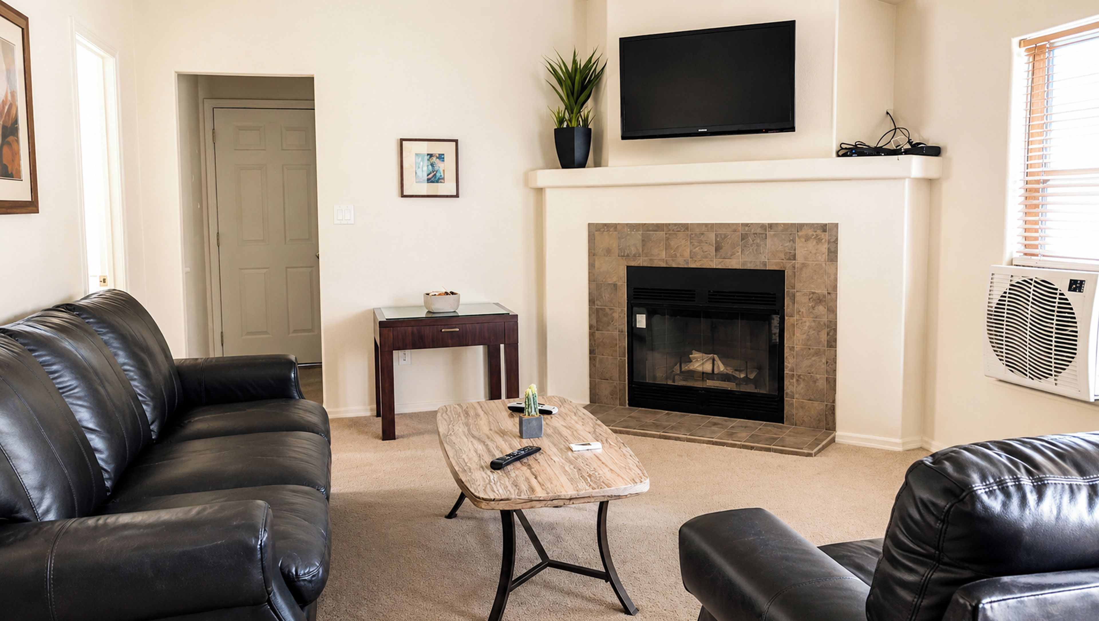 A living room with a fireplace, leather sofas, a coffee table, and a TV mounted on the wall.