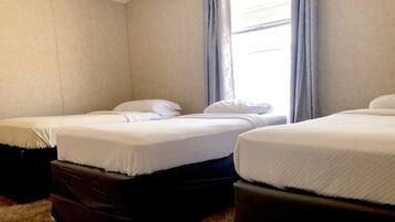 Two single beds with matching pillows and duvets, set in a spacious room with a large window and carpeted floor.