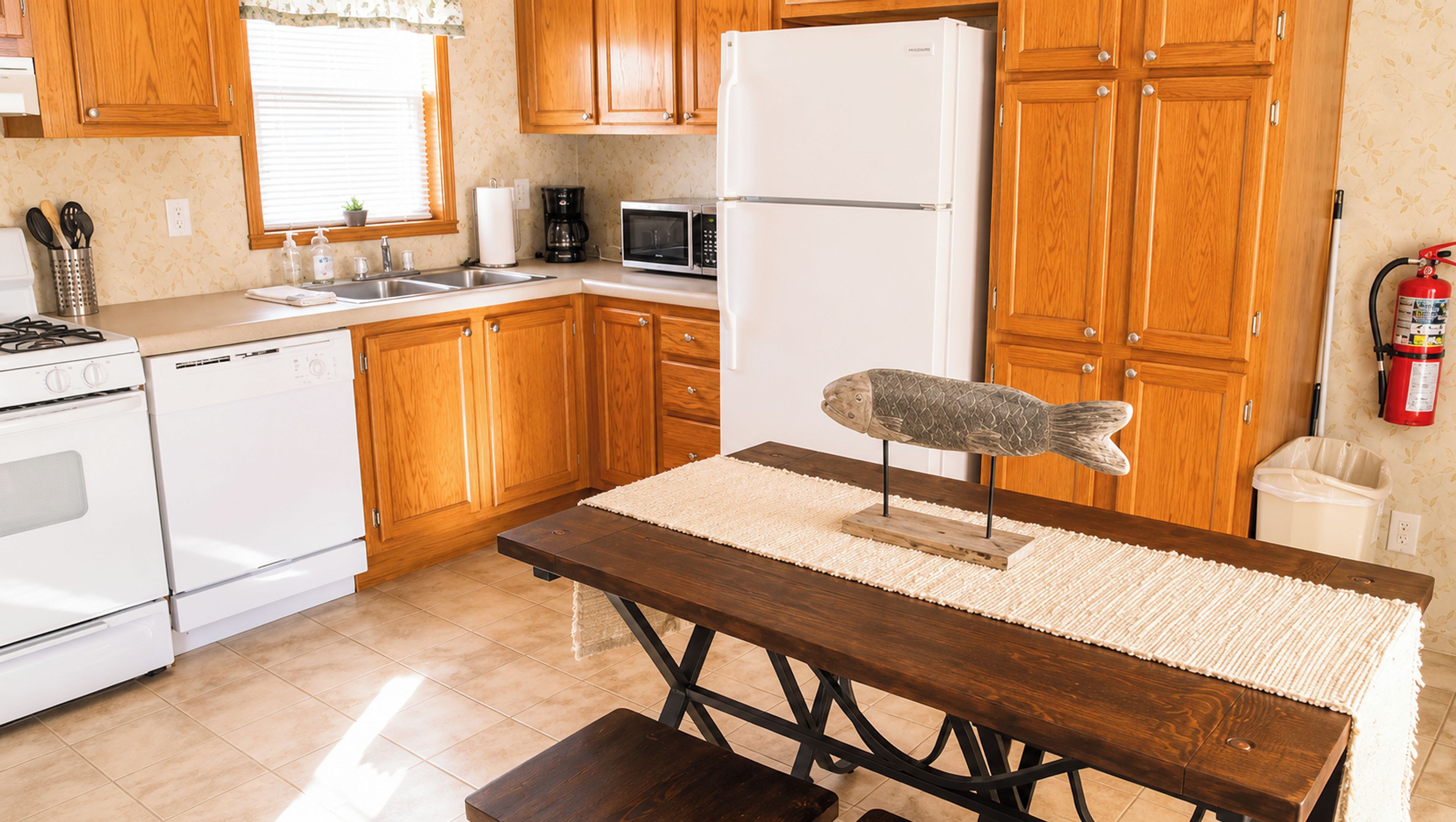 Una cocina con armarios de madera, un refrigerador blanco, un microondas y una decoración con forma de pez sobre la mesa.