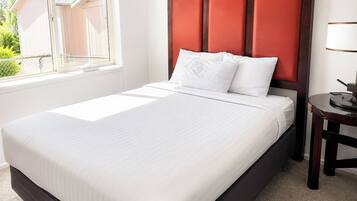 Una cama bien hecha con ropa blanca en una habitación con ventana y una mesita de noche.
