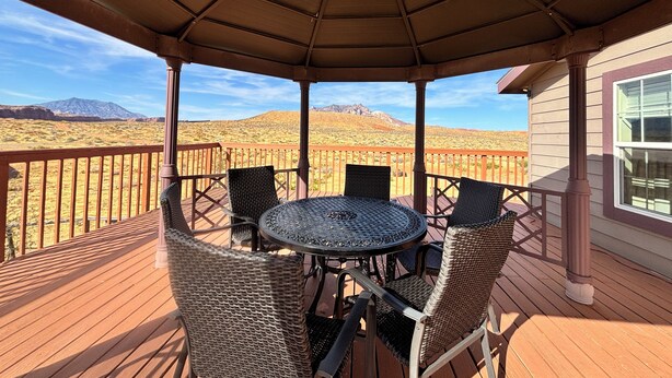 Un espace extérieur aménagé, abrité et doté d’une table et de chaises, offrant une vue sur un paysage désertique et montagneux.