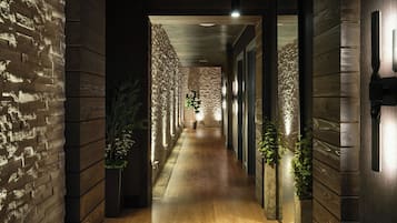 A corridor with wooden walls and a wooden floor, leading to a room with a stone wall and a plant.