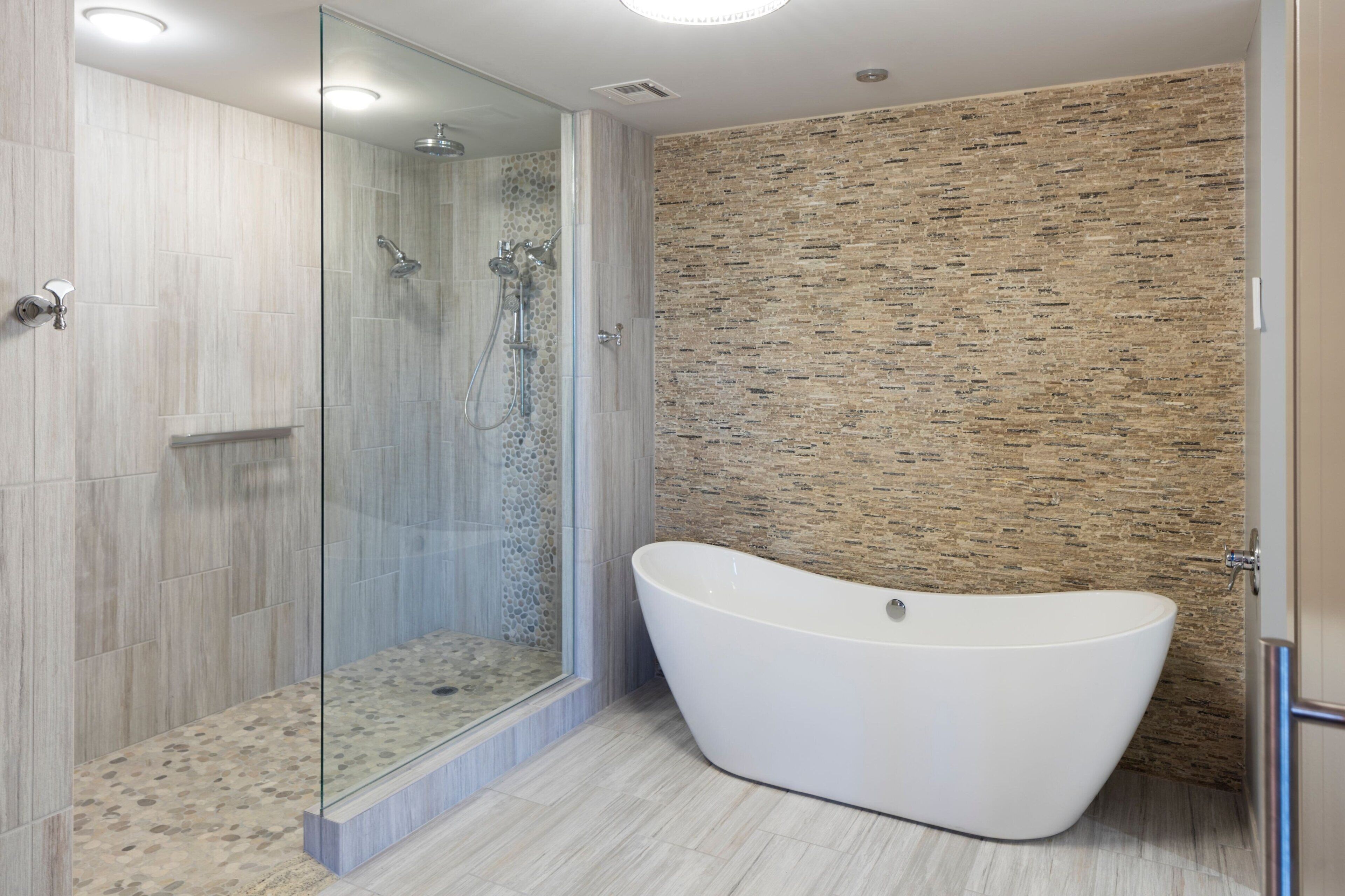 Un baño moderno con una bañera independiente, ducha con cerramiento de vidrio y pared con textura.