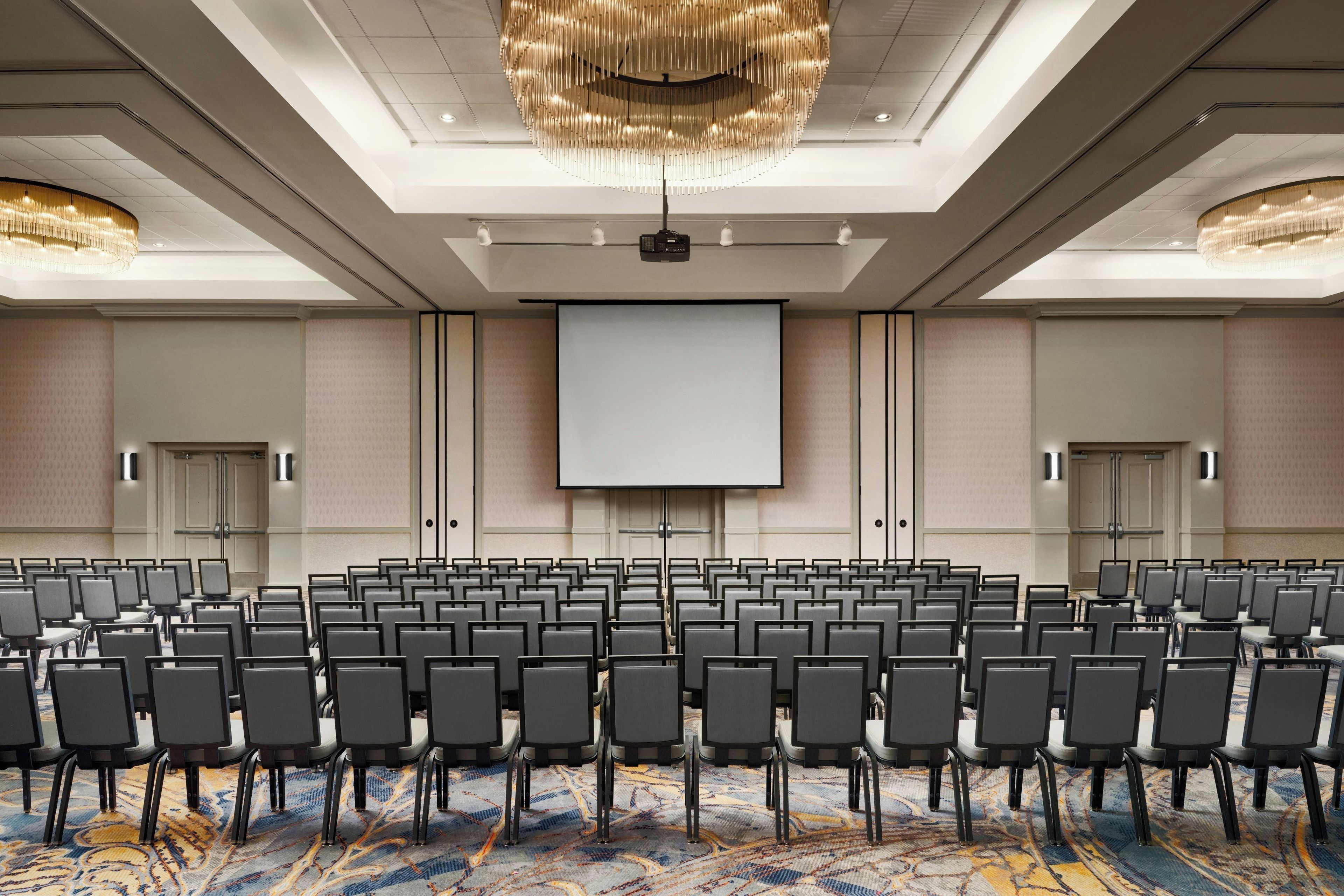 A conference room with rows of chairs, a large screen, and a projector.