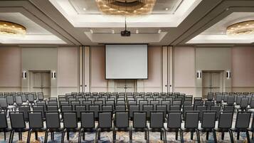 A conference room with rows of chairs, a large screen, and a projector.