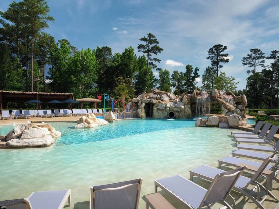 A pool area with lounge chairs, a water feature, and a naturalistic rock formation.